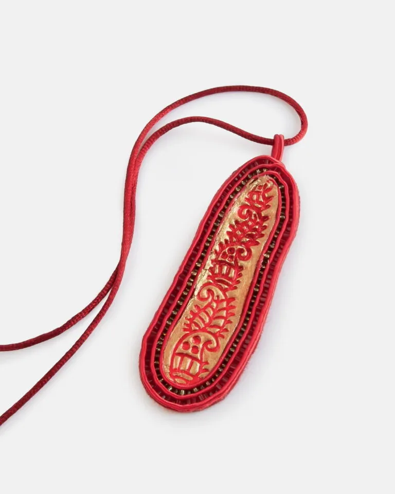 Czerwono-złoty haftowany amulet z chińskimi znakami, zawieszony na czerwonym sznurku, przedstawiony na białym tle.