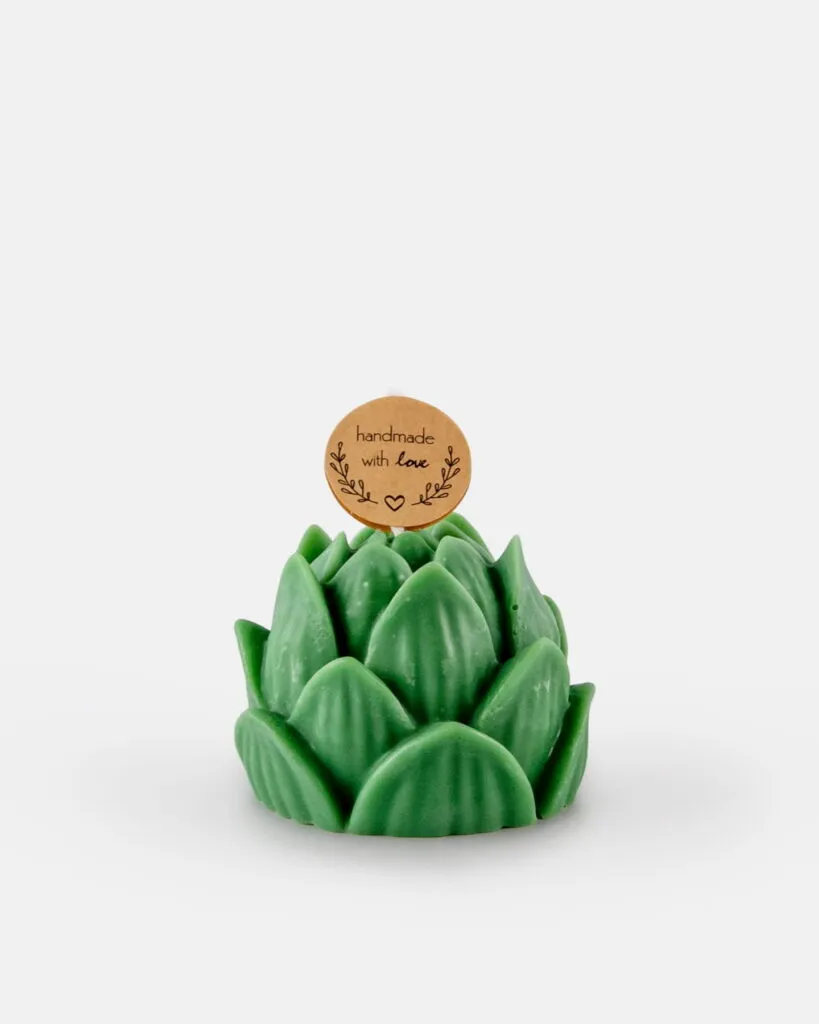 Świeczka sojowa w kształcie zielonej rośliny sukulentowej, ozdobiona małą, okrągłą karteczką z napisem „handmade with love” oraz prostymi rysunkami liści, umieszczona na białym tle.