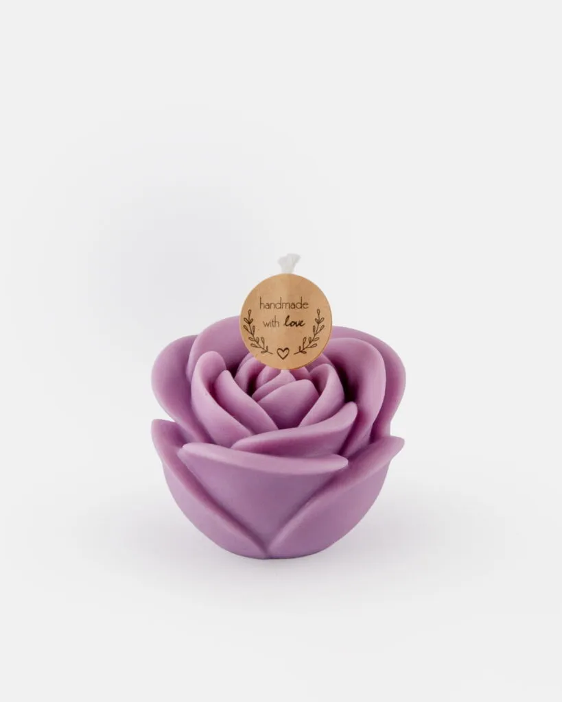 Świeczka sojowa w kształcie róży, w kolorze lawendowym, z okrągłą zawieszką z napisem „handmade with love” przymocowaną do knota, umieszczona na białym tle.