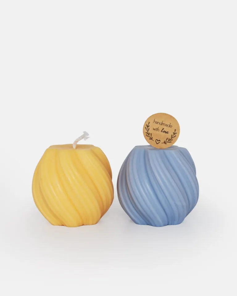 Dwie okrągłe świece z żłobieniami: jedna żółta z białym knotem, a druga niebieska z korkową zawieszką z napisem „handmade with love” na gładkim białym tle.