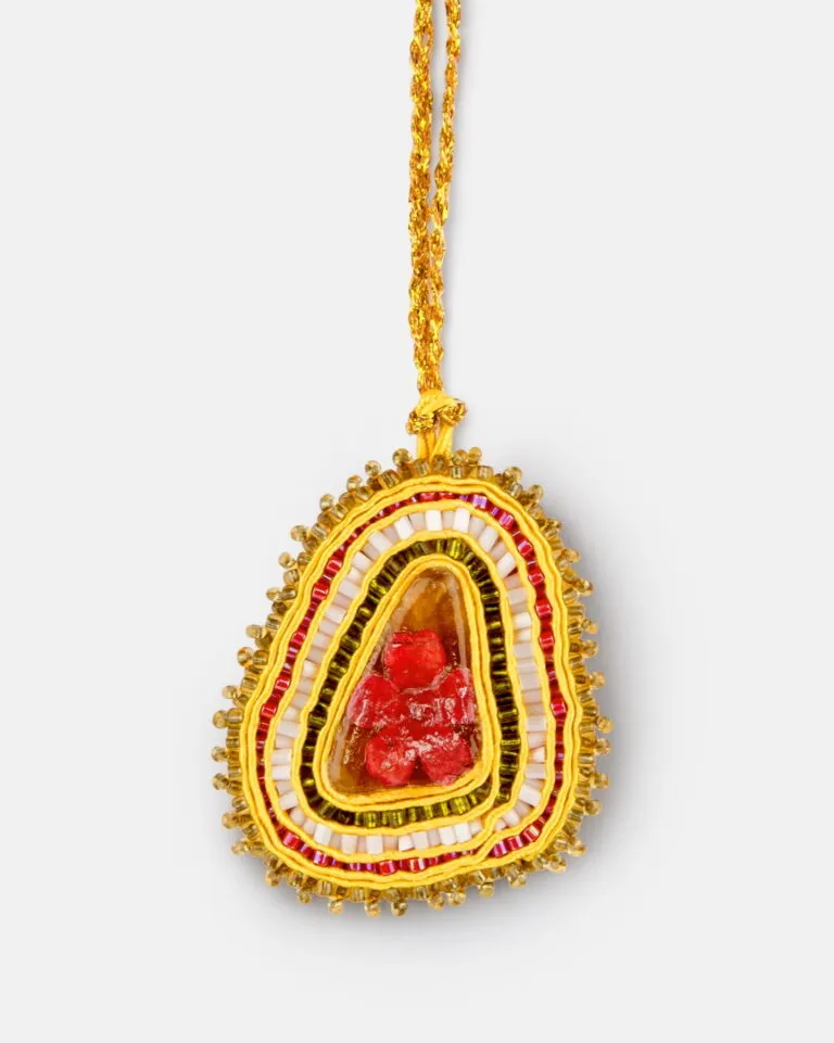 Wisiorek z koralików na żółtym sznurku, z czerwonym kamieniem pośrodku, otoczonym warstwami żółtych, białych i czerwonych koralików typu seed beads.