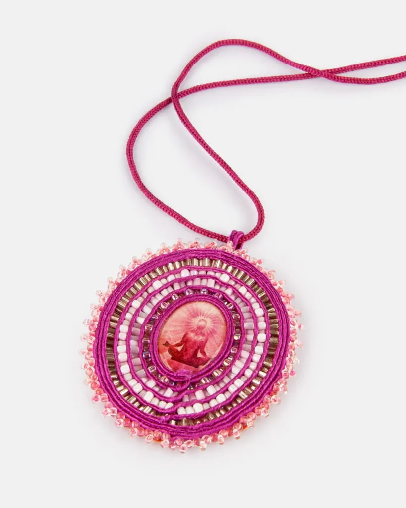 Okrągły wisiorek z koralików na sznurku w kolorze magenta, z centralnym wizerunkiem osoby siedzącej w pozycji medytacyjnej.